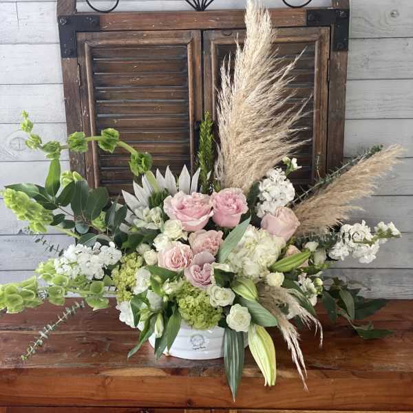 Arrangement of pink and white flowers in a white container with pampas grass