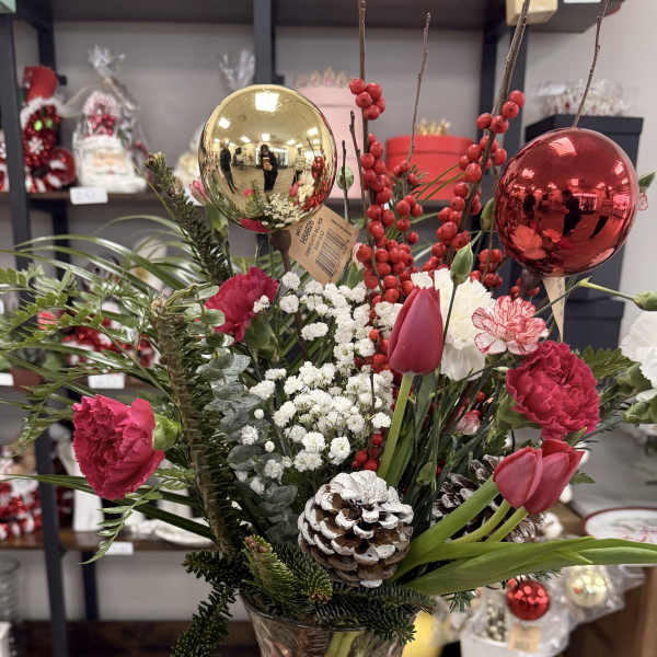 Holiday bouquet in a glass vase with red flowers, berries, and ornaments