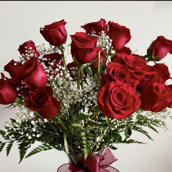 Red roses arranged in a clear glass vase with baby's breath and a burgundy ribbon