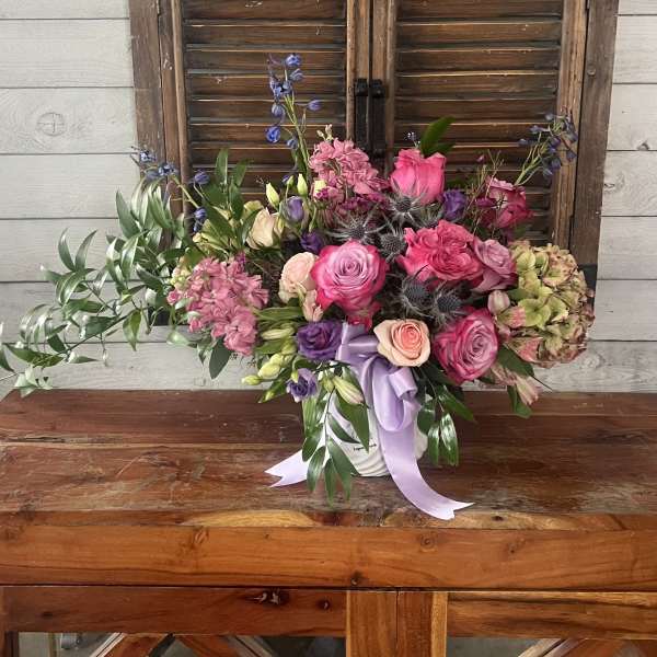 Pink and purple mixed flower arrangement in a white container with ribbon