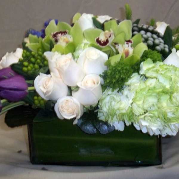 Mixed bouquet with white roses, green orchids, and purple tulips in a rectangular vase