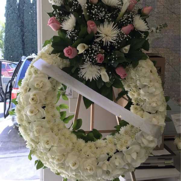 Large white floral wreath with pink roses and a ribbon sash