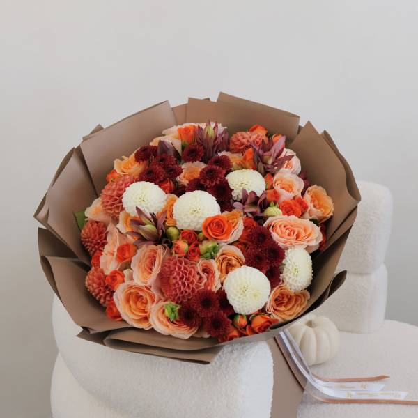 Bouquet of orange, peach, white, and burgundy flowers wrapped in brown paper