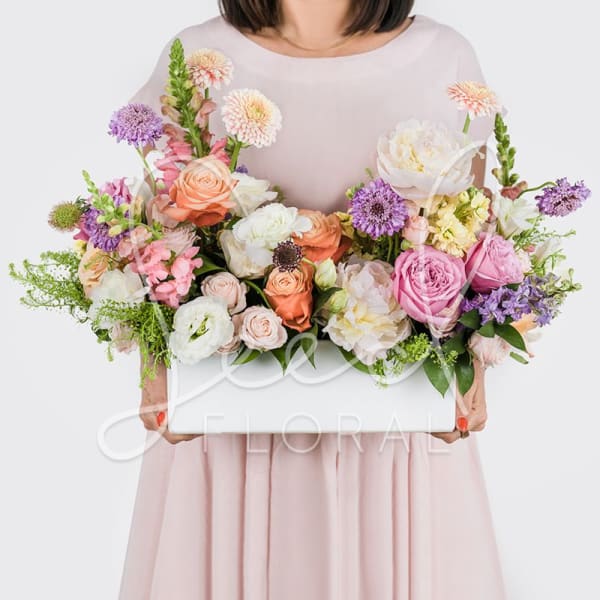 Woman holding a large pastel flower arrangement in a white box