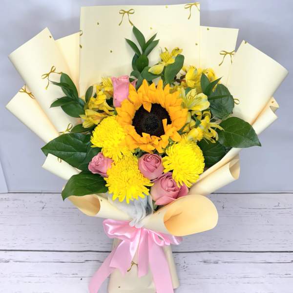 Bouquet of yellow sunflowers, pink roses, and yellow mums wrapped in cream paper