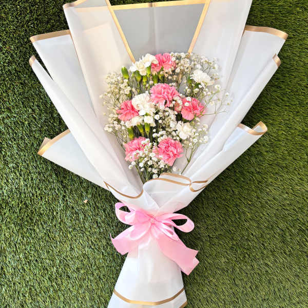 Pink and white carnation bouquet wrapped in white paper with a pink ribbon
