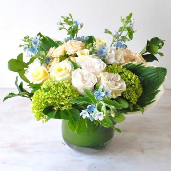 Bouquet of cream roses and blue flowers in a green glass vase