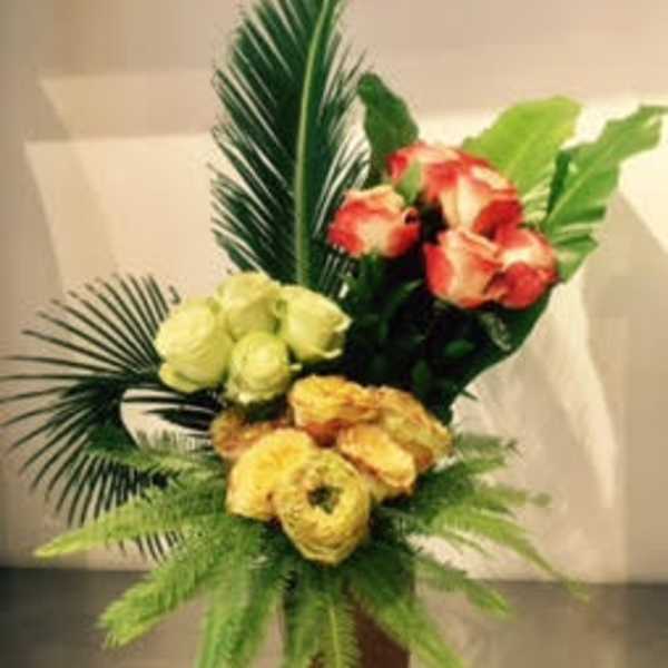 Bouquet of yellow, red, and white flowers in a vase with tropical leaves