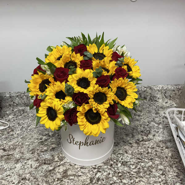 Bouquet of yellow sunflowers and red roses in a white hatbox
