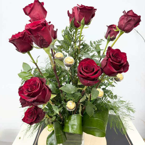 Red roses arranged in a clear square vase with greenery