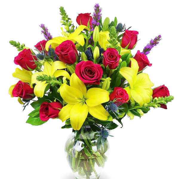 Bouquet of yellow lilies and red roses with purple accents in a clear glass vase