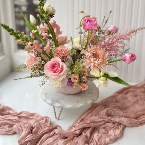 Pink and peach floral arrangement in a low vase on a pedestal