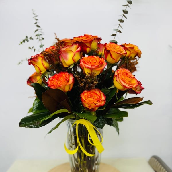 Bouquet of orange and yellow roses in a clear glass vase with a yellow ribbon