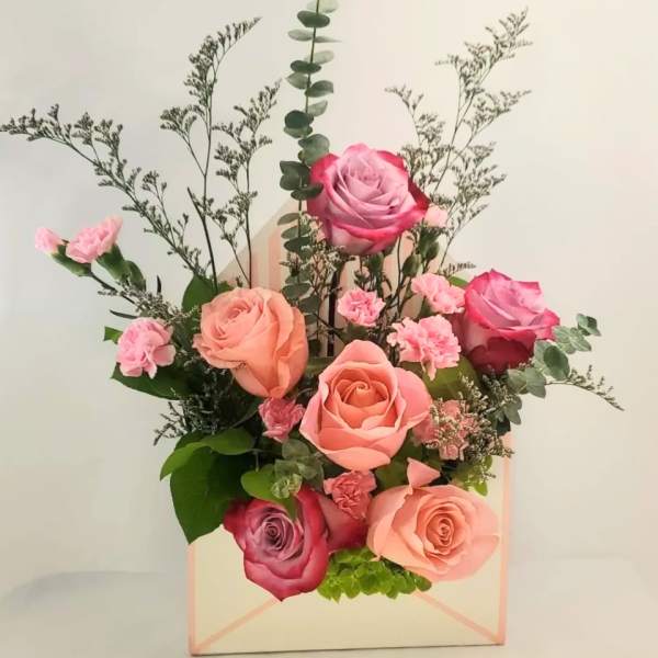 Pink and peach roses arranged in a pastel gift box with greenery