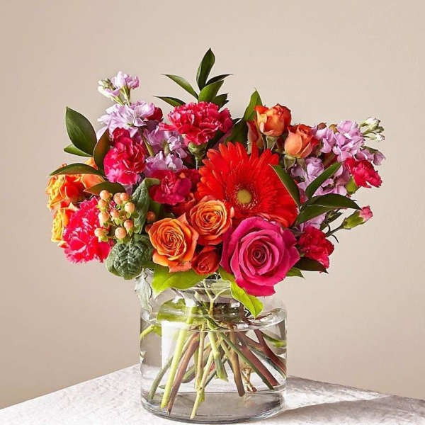 Mixed bouquet of roses, gerbera daisies, and carnations in a clear glass vase
