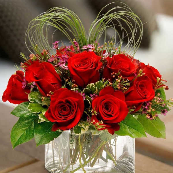 Red roses arranged in a clear square glass vase with decorative loops