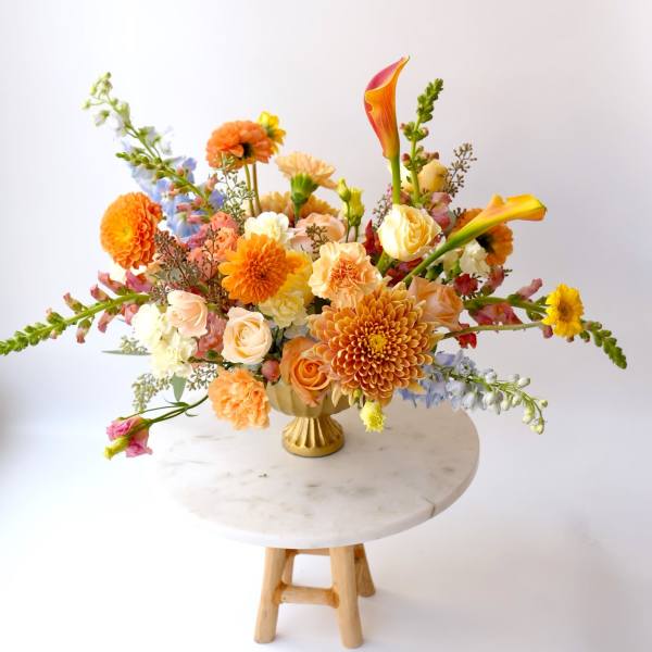 Colorful mixed flower arrangement in a gold vase on a round table