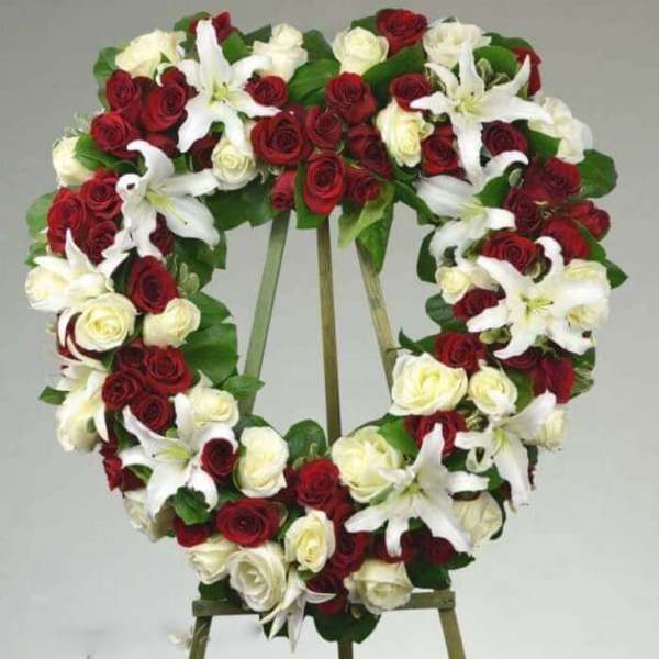 Heart-shaped wreath of red and white roses with white lilies on an easel