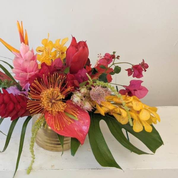 Tropical bouquet with red, pink, and yellow flowers in a gold vase