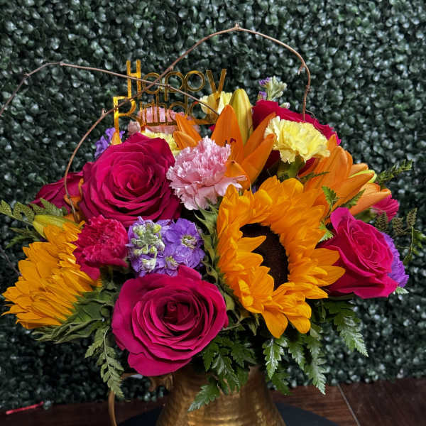 Bright mixed bouquet in a gold pitcher vase with a birthday topper