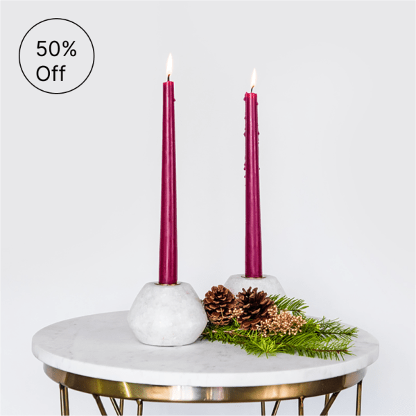Pair of tall burgundy taper candles in white holders on a round marble table