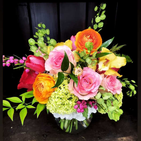 Colorful bouquet of roses, ranunculus, and orchids in a glass vase