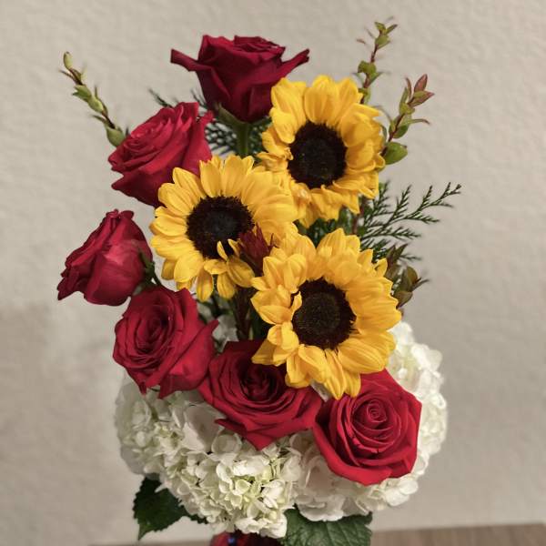 Red roses and yellow sunflowers in a red vase with white hydrangeas