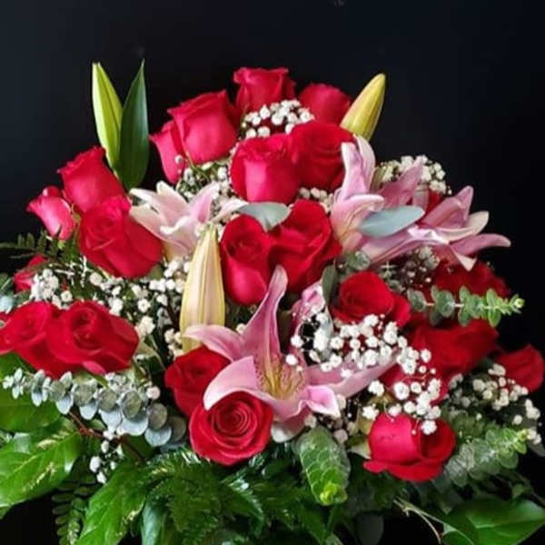 Tall glass vase of red roses, pink lilies, and white filler flowers in a full rounded bouquet