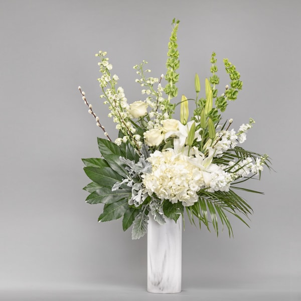 White floral arrangement in a tall marble vase with green accents