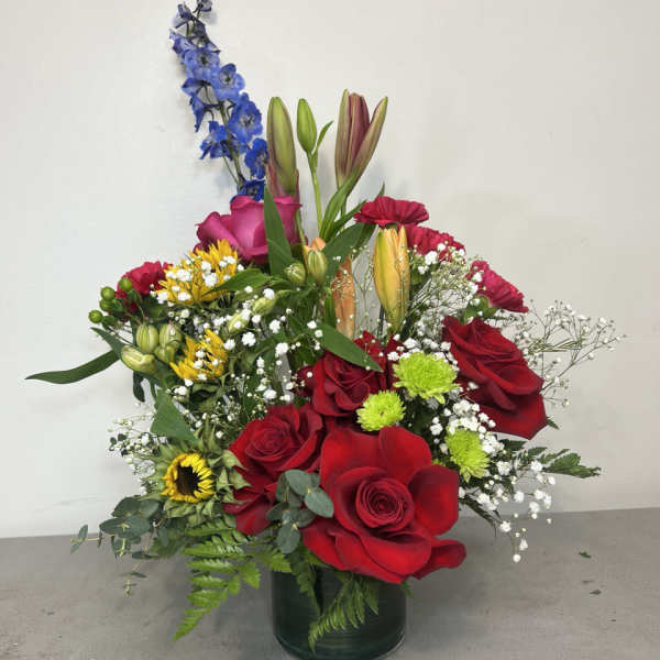 Mixed bouquet of red roses, lilies, and blue delphinium in a glass vase