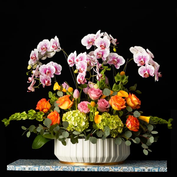 Mixed floral arrangement with orchids, roses, and hydrangeas in a white vase