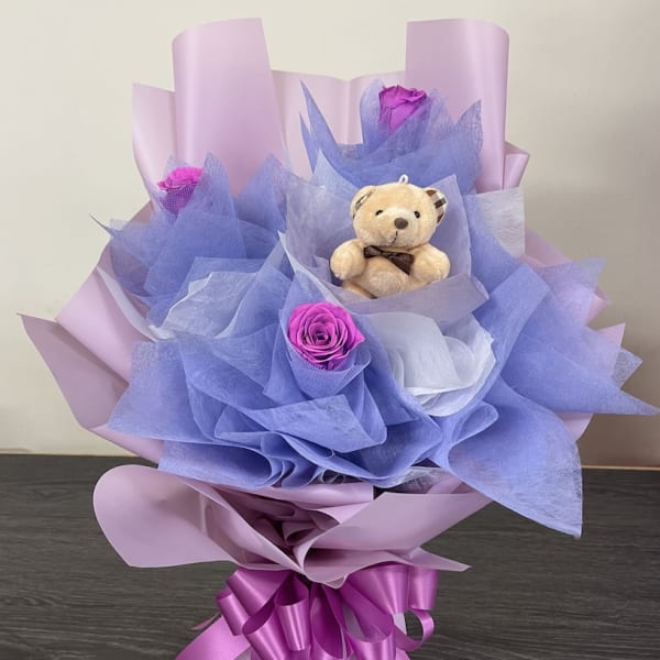 Bouquet with purple roses and a small teddy bear wrapped in pink and blue paper