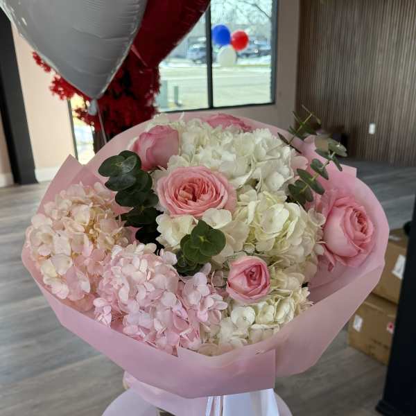 Pink and white bouquet of roses and hydrangeas wrapped in pink paper