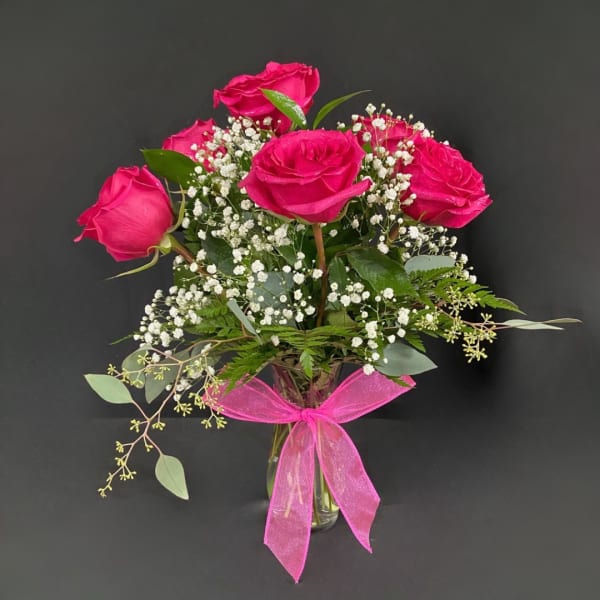Pink roses in a clear glass vase with baby's breath and a pink ribbon