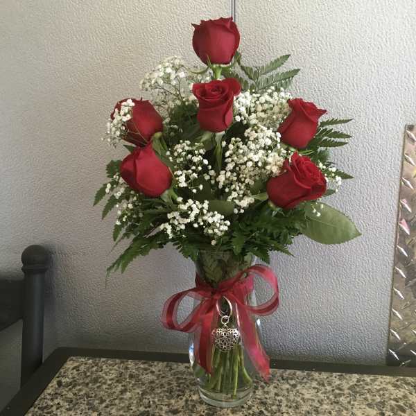 Tall arrangement of red roses and white filler flowers in a clear vase with a red bow