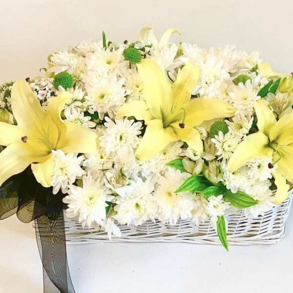 Yellow lilies and white daisies in a white basket with a black ribbon