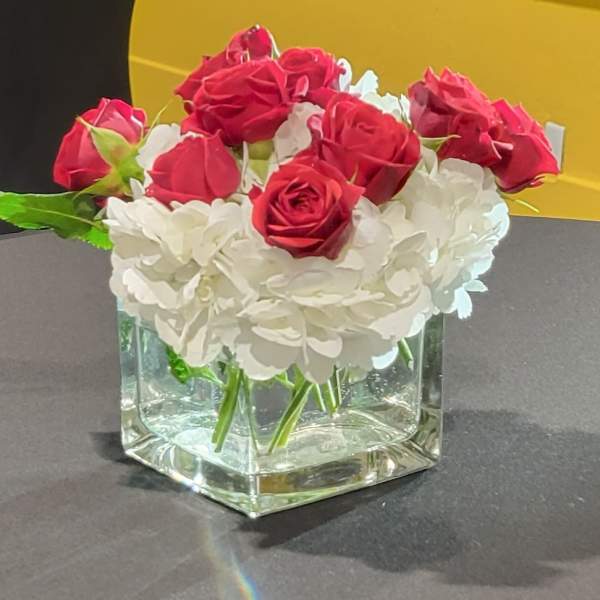 Red roses and white hydrangeas arranged in a clear square vase.