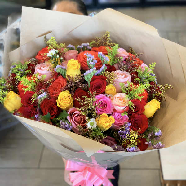 Bouquet of multicolored roses wrapped in brown paper with a pink ribbon