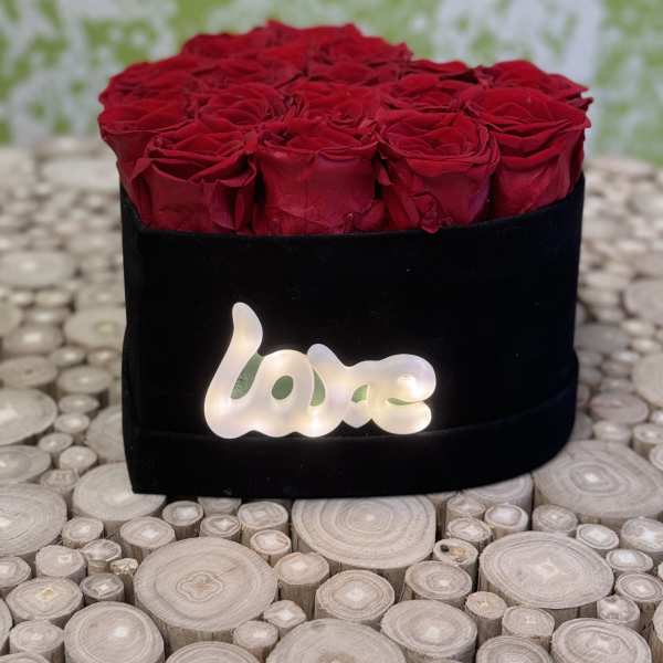Red roses arranged in a black box with a glowing "love" sign