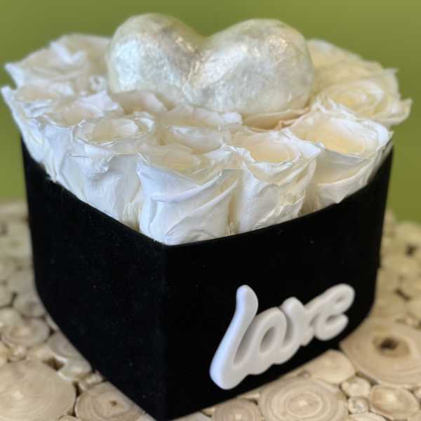 White roses in a black heart-shaped box with a silver heart topper