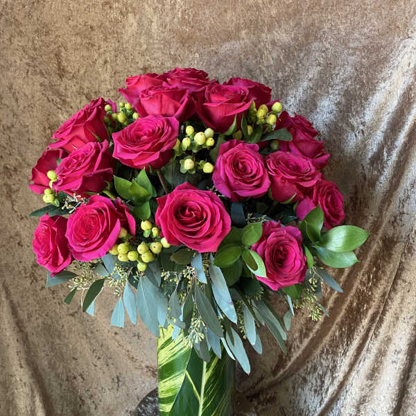 Hot pink roses in a glass vase with green berries and foliage