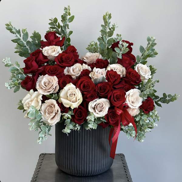 Red and blush roses arranged in a black vase with eucalyptus