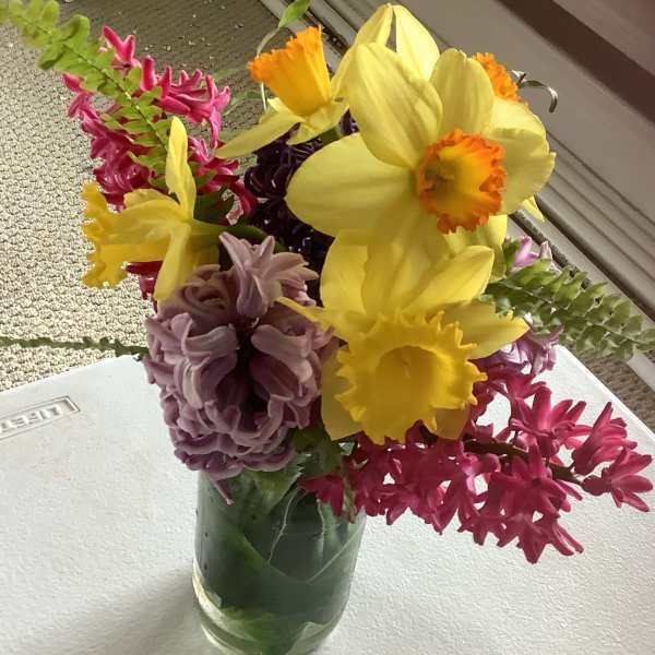Bouquet of yellow daffodils, pink hyacinths, and purple blooms in a glass vase