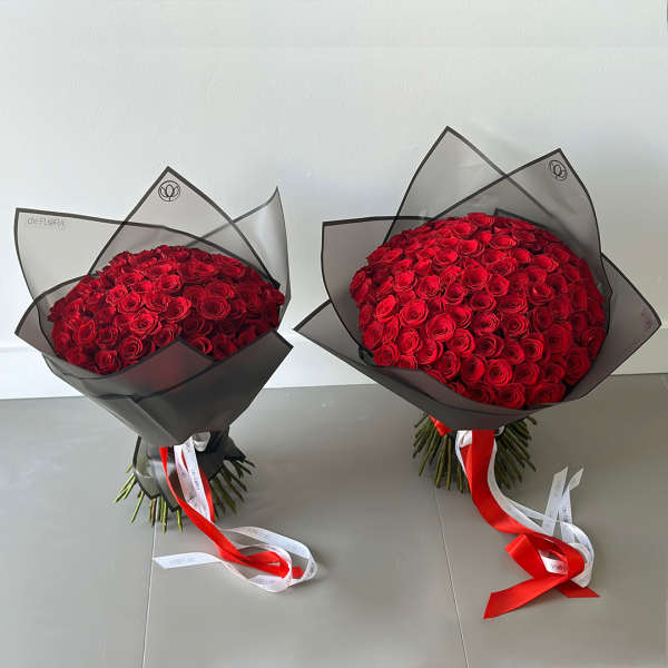 Two large bouquets of red roses wrapped in black translucent paper with long red and white ribbons.