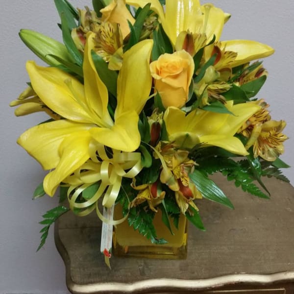 Yellow lilies and roses in a square glass vase