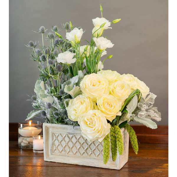 Cream roses and white blooms in a rectangular planter with candles nearby