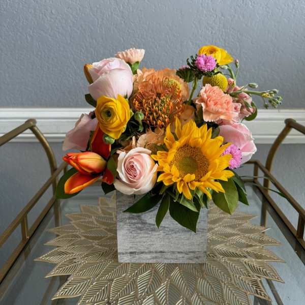 Mixed bouquet with sunflowers, roses, and carnations in a square vase