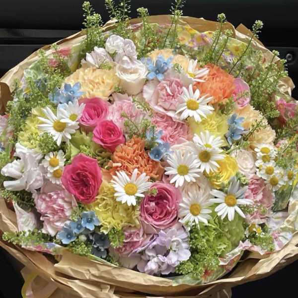 Mixed bouquet of pastel flowers with daisies and roses wrapped in brown paper