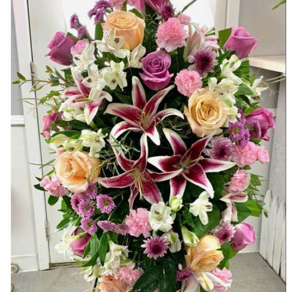 Standing floral spray with pink and peach roses and lilies on a black easel