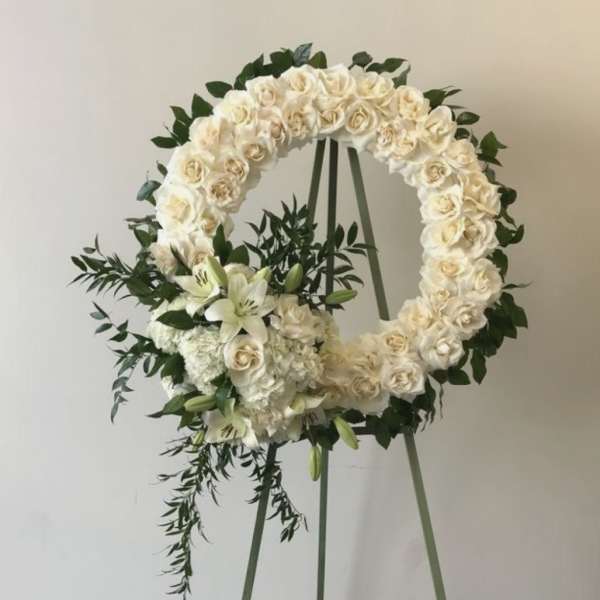 White rose wreath on an easel with lilies and greenery